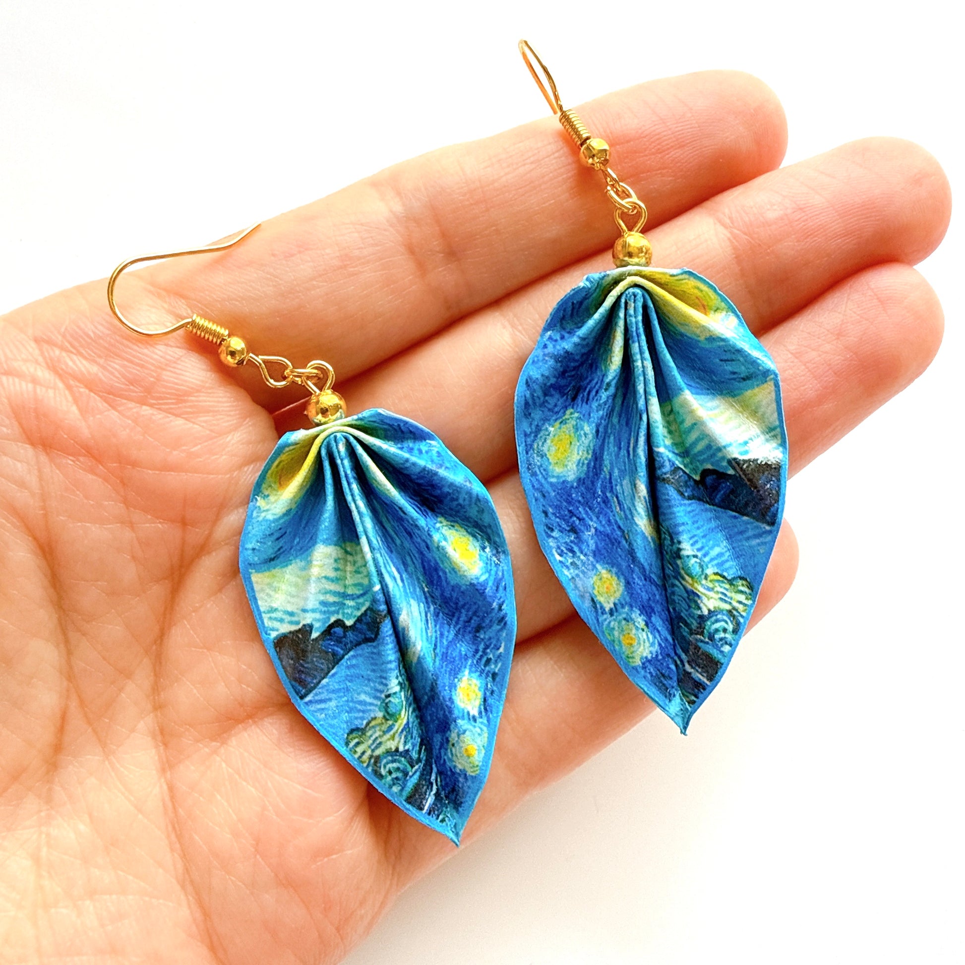 Blue floral-patterned earrings held in a hand against a white background