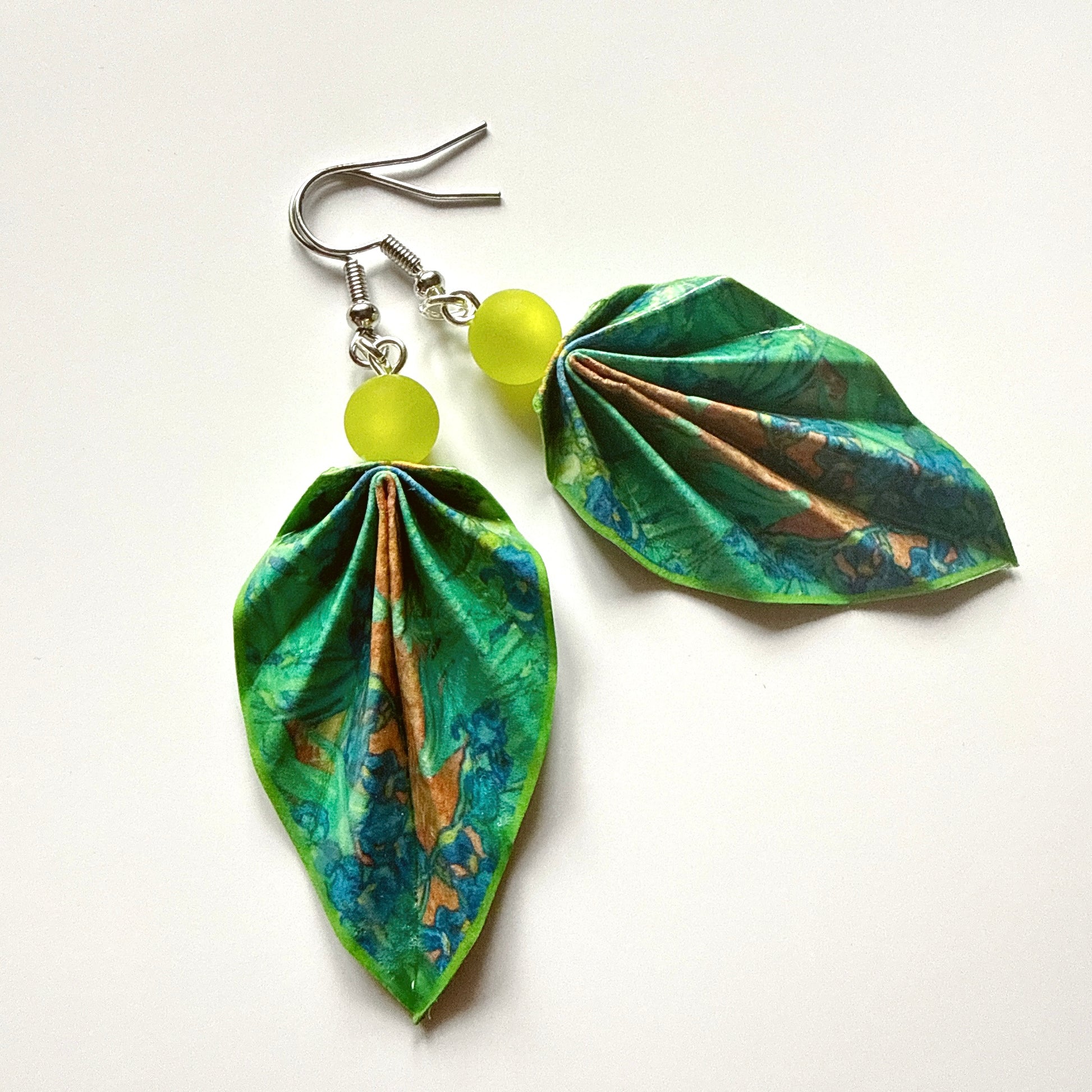Leaf-shaped earrings with green and blue patterns and yellow beads on a white background