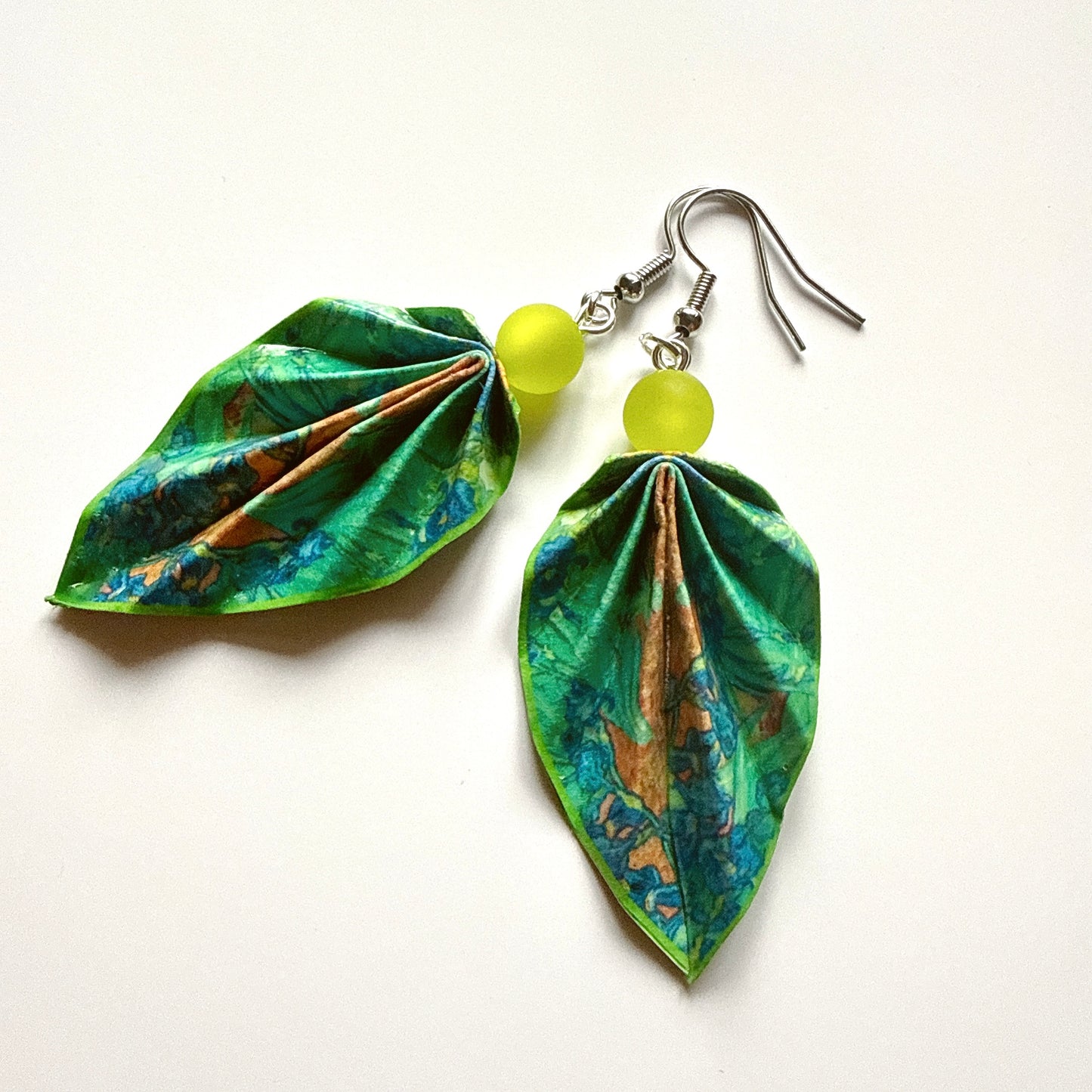 Leaf-shaped earrings with green and blue patterns and yellow beads on a white background