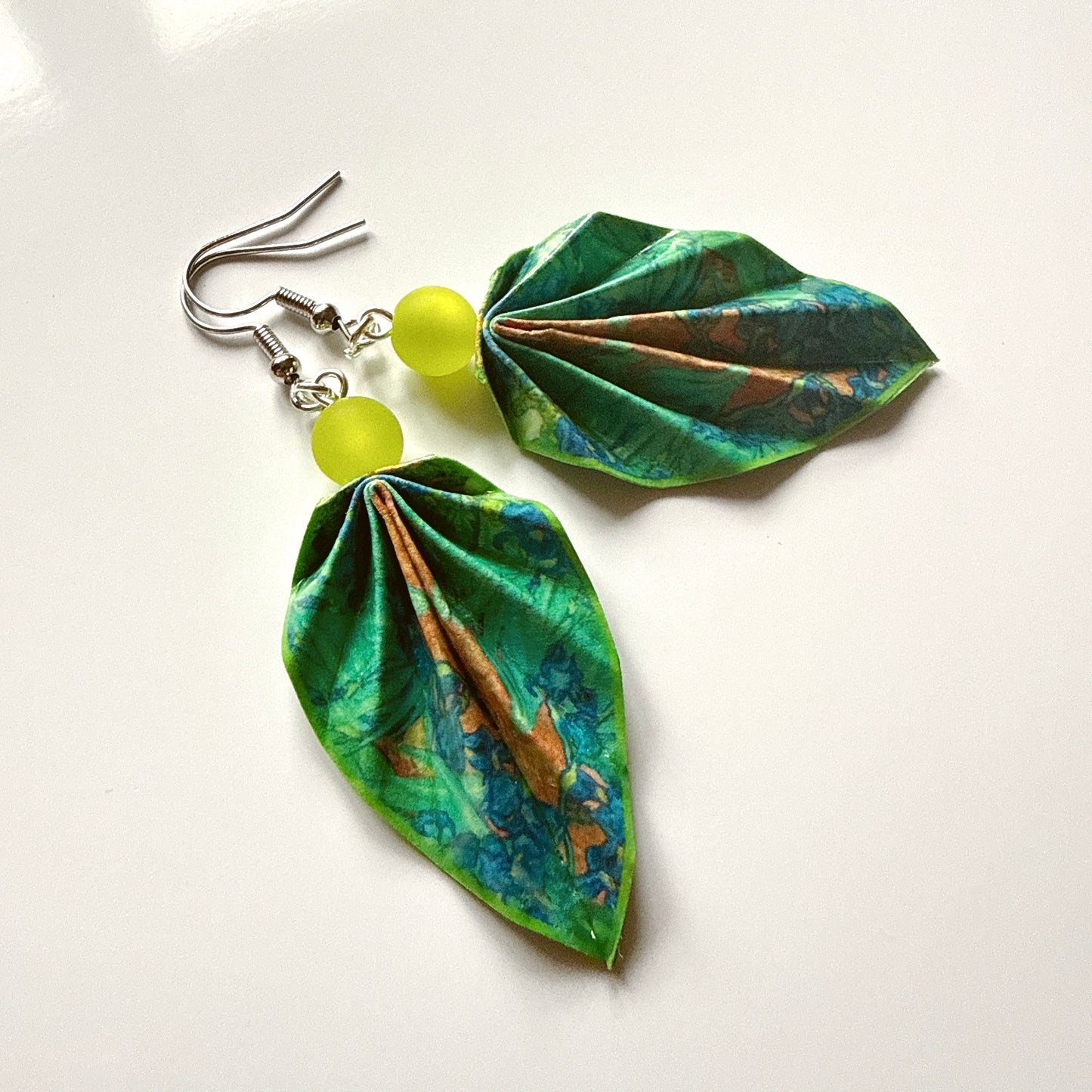 Leaf-shaped earrings with green and blue patterns and yellow beads on a white background