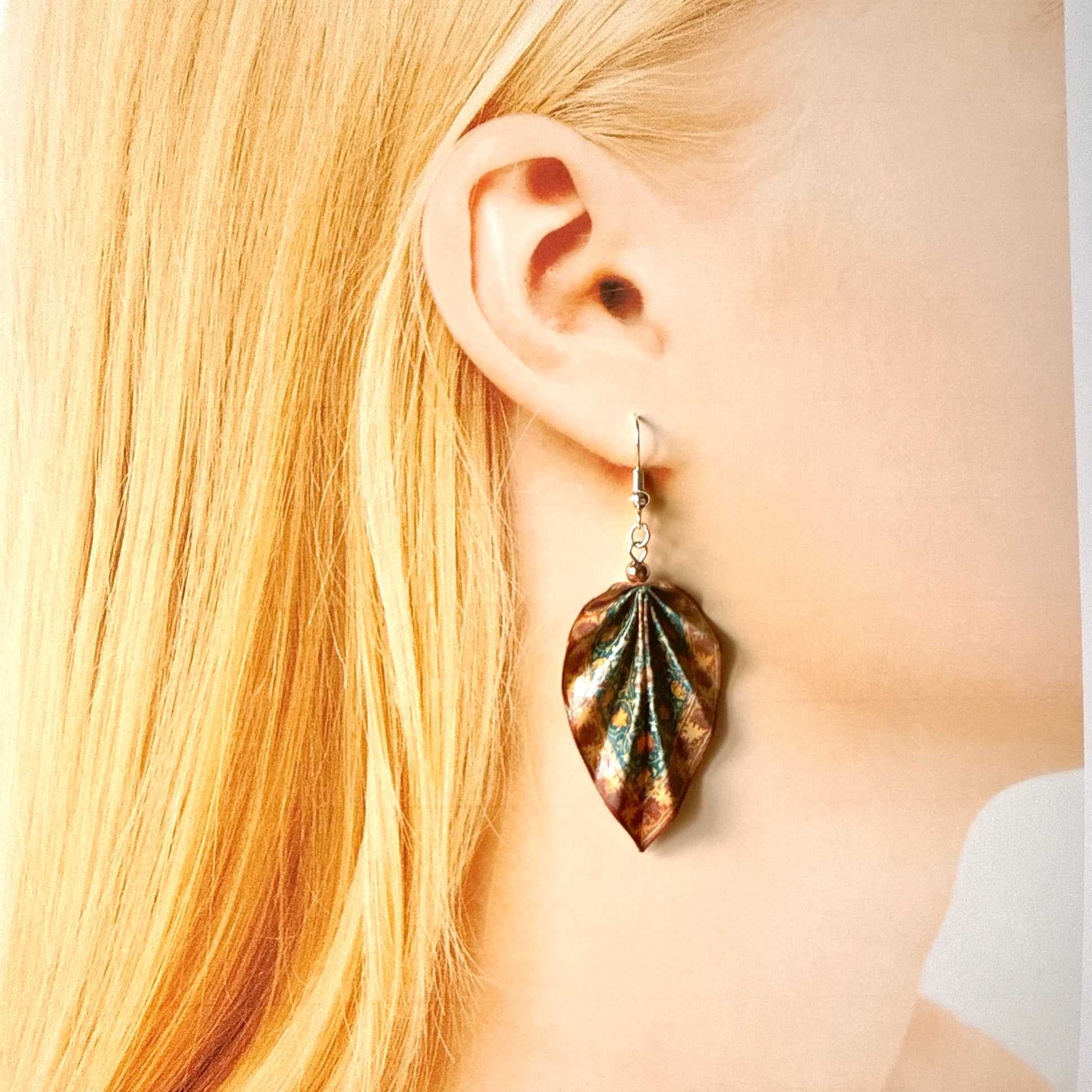 Close-up of a person wearing a leaf-shaped earring with a blurred background