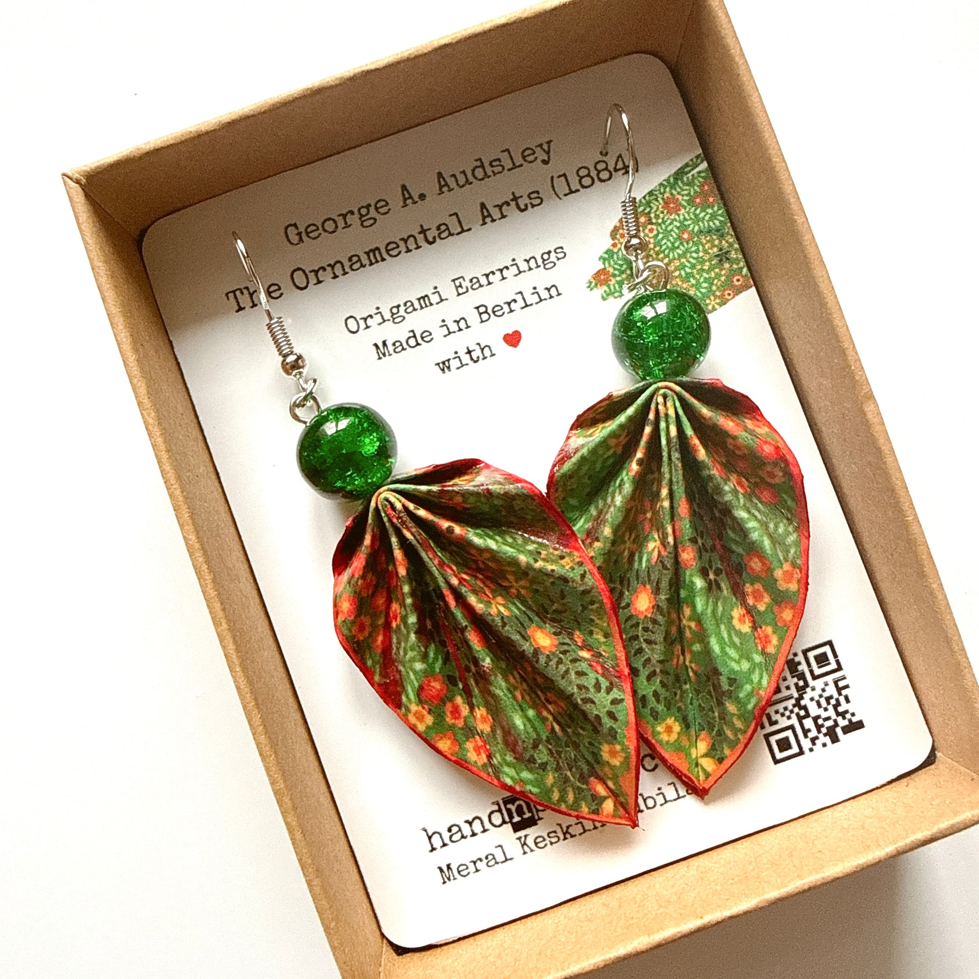 Origami earrings with green and red patterns in a box with a card.