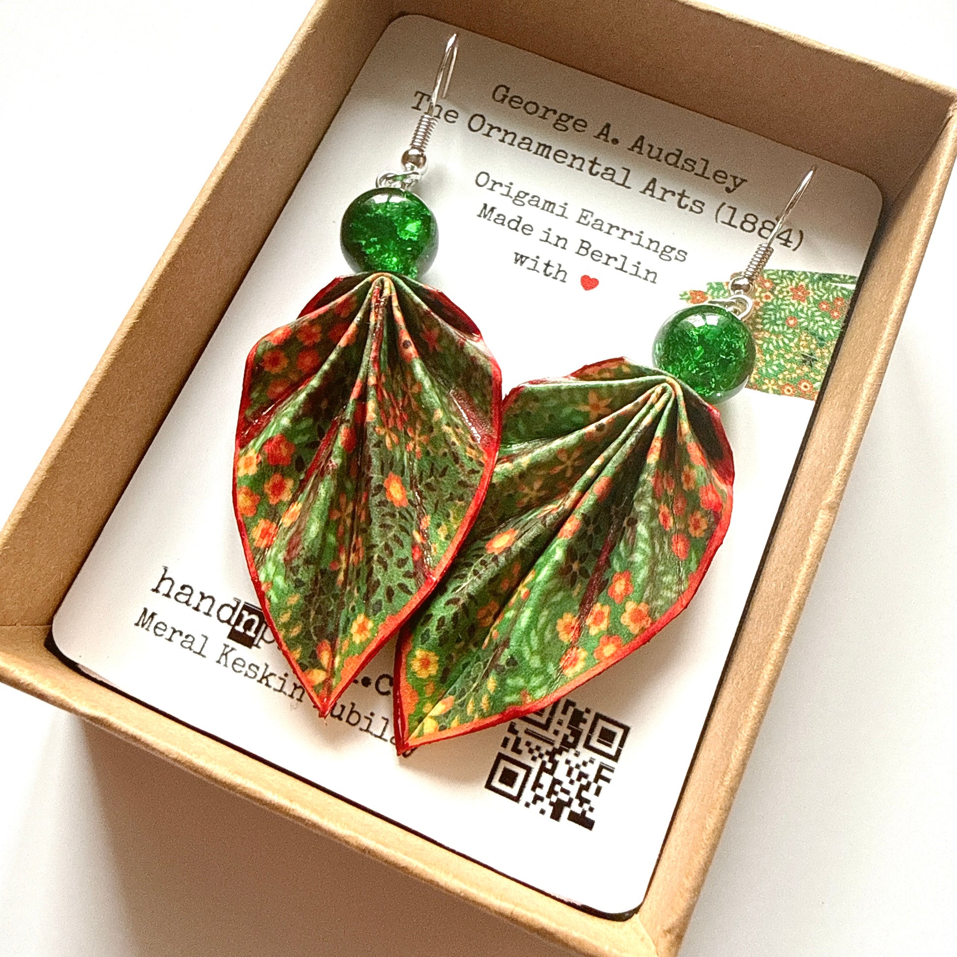 Origami earrings with green and red patterns in a box with a label.