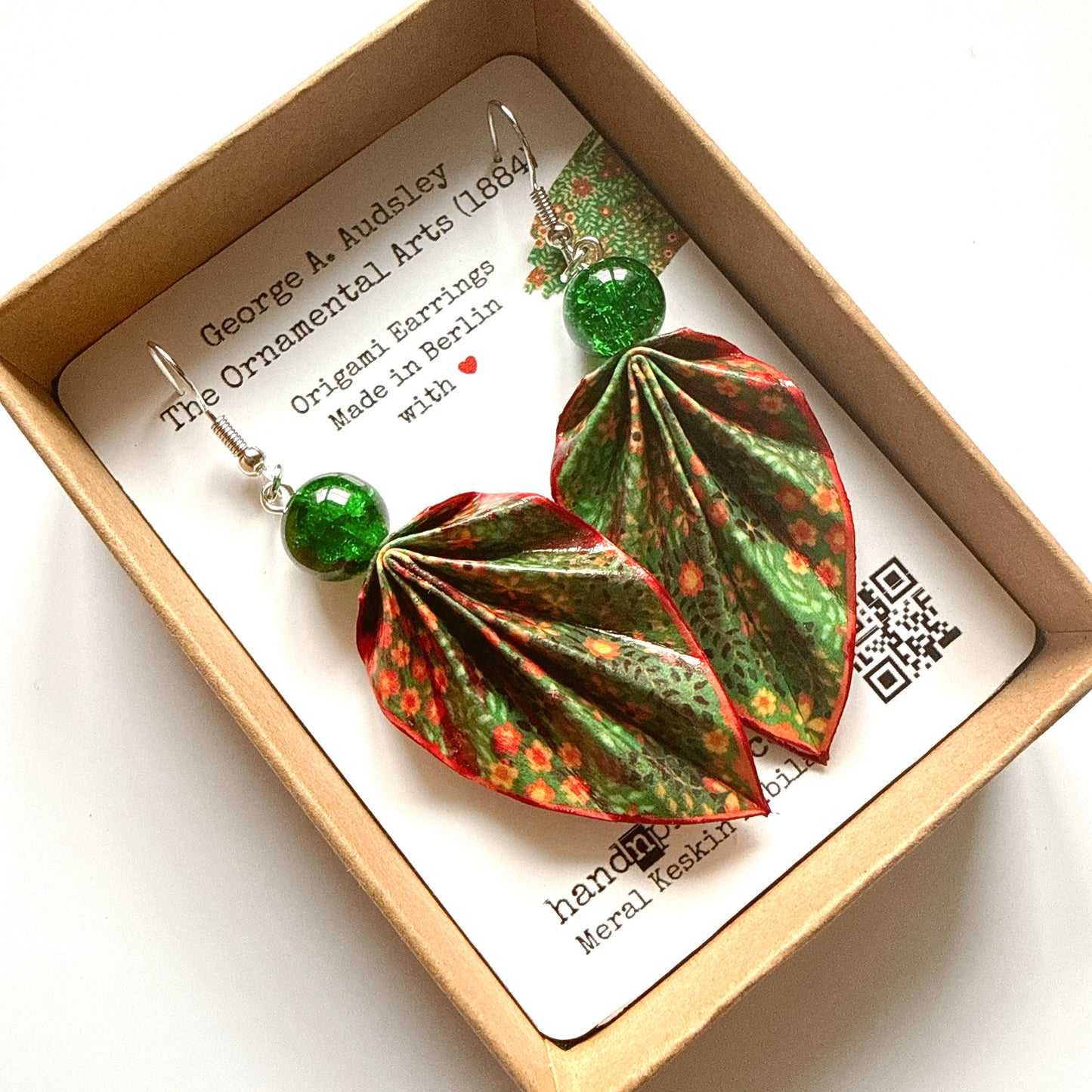 Pair of origami leaf earrings with green beads in a box with a label.