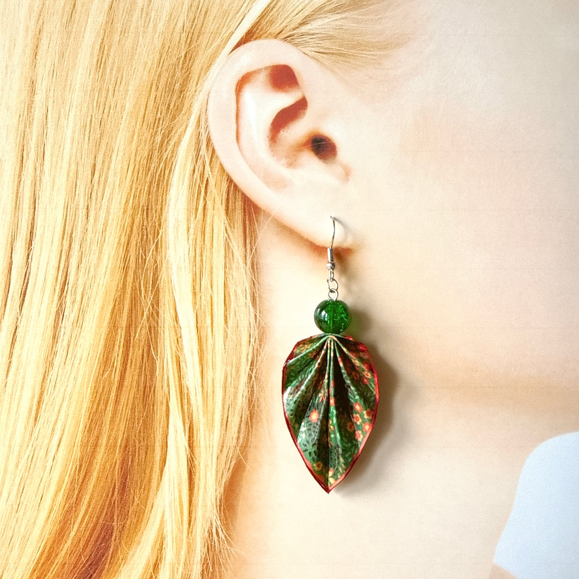 Close-up of a person wearing a green and red leaf-shaped earring.