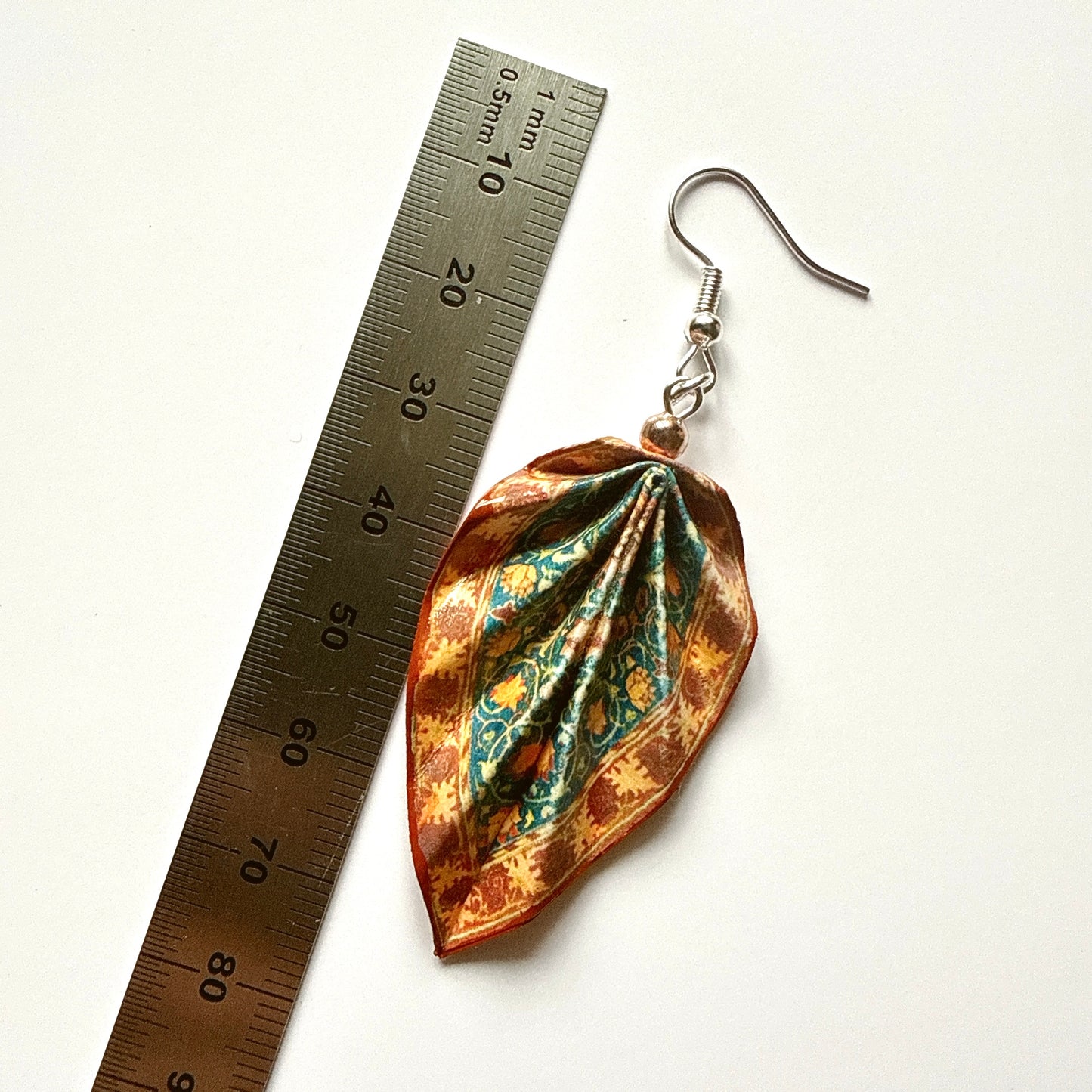 Decorative earring with floral pattern next to a ruler on a white background