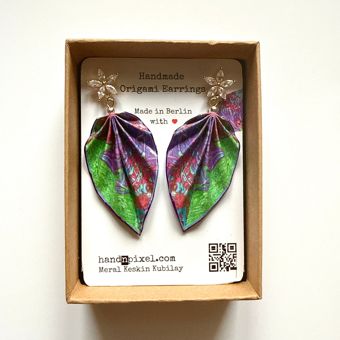 Handmade origami earrings in a box with branding information.