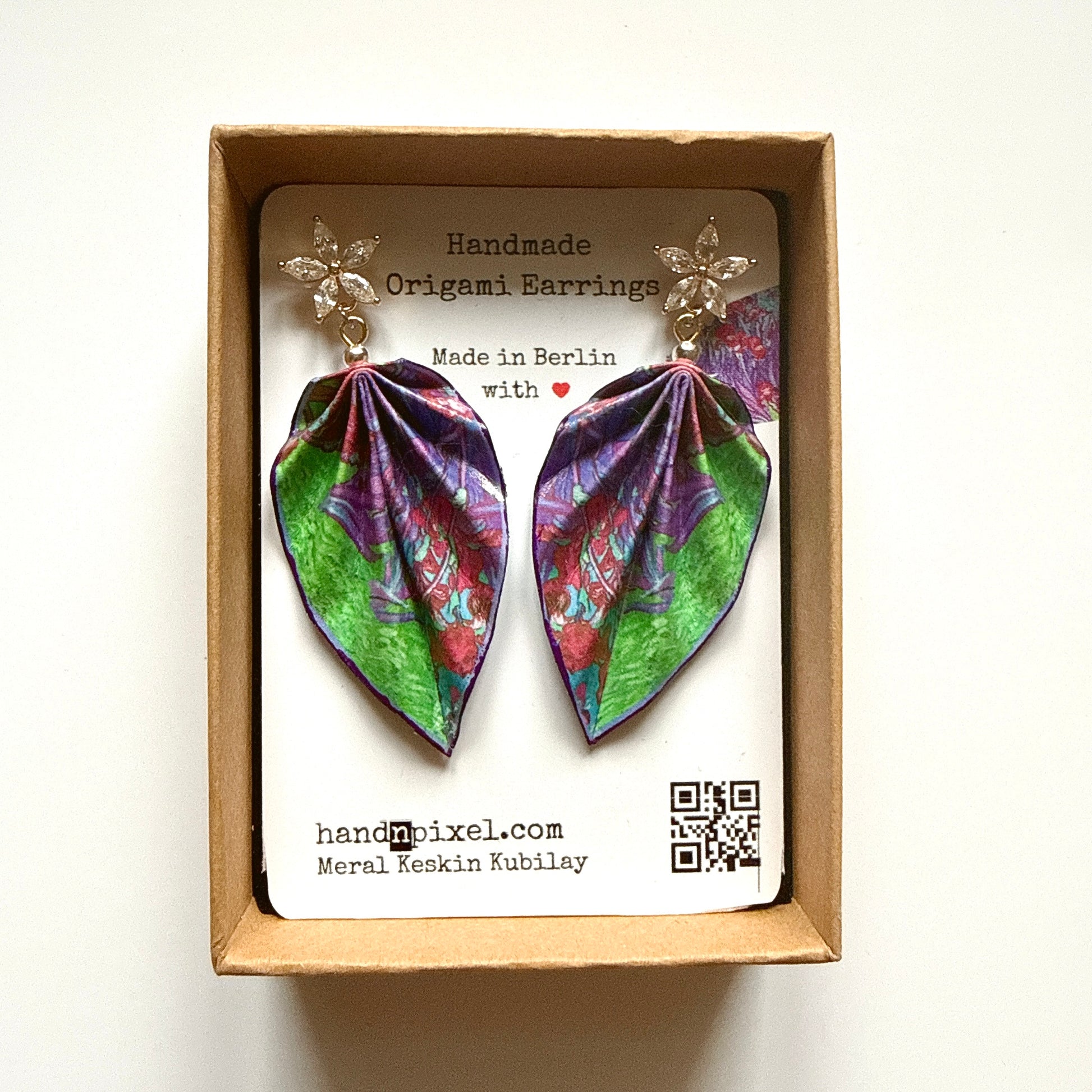 Handmade origami earrings in a box with branding information.