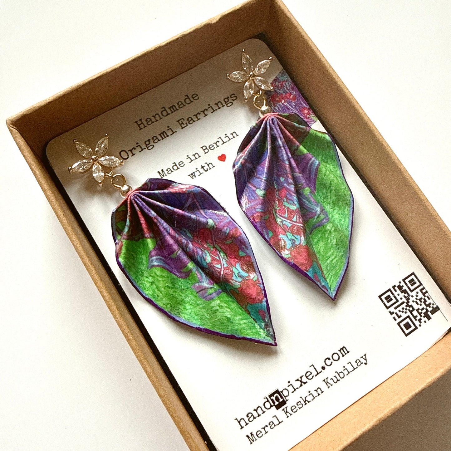 Handmade origami earrings in a box with branding information.