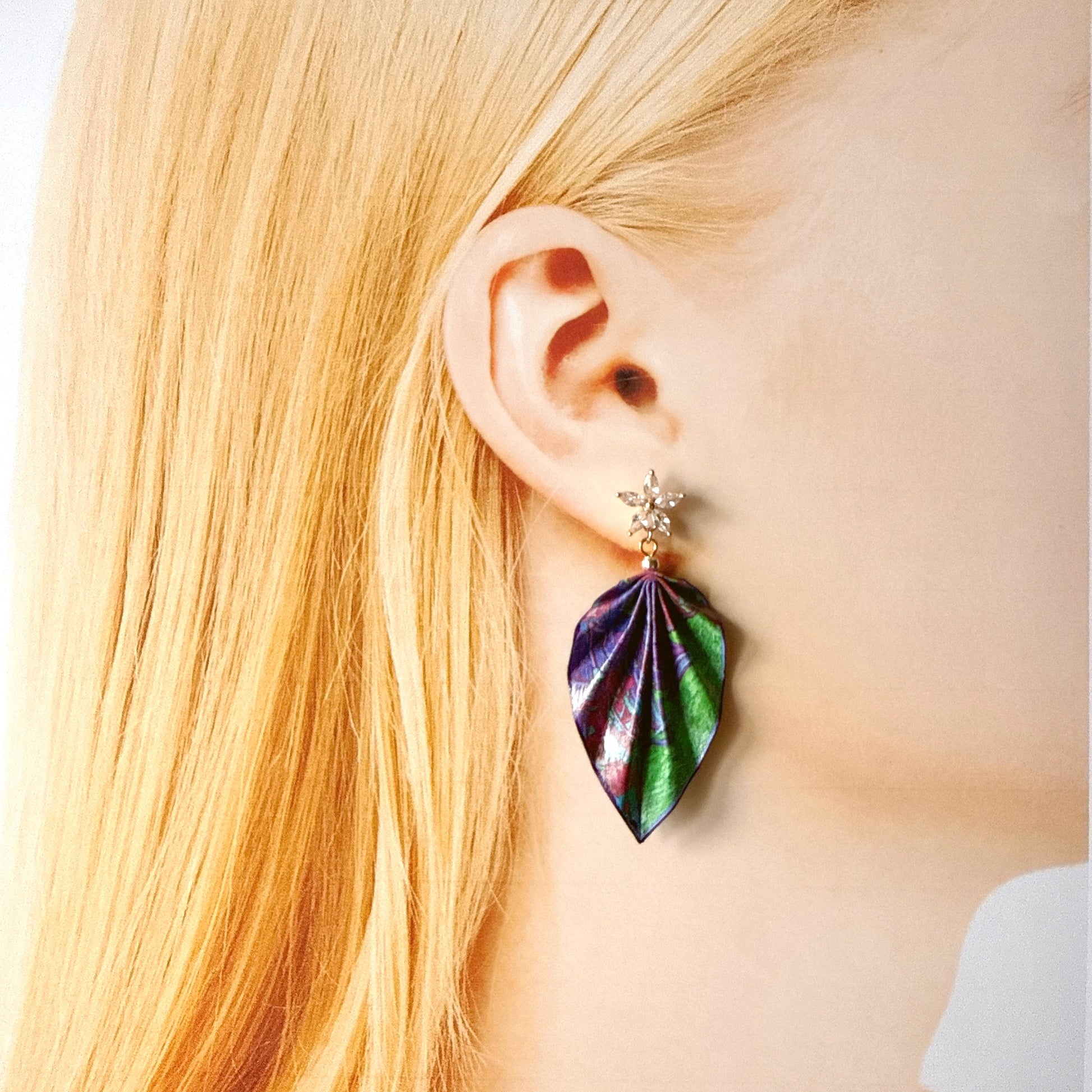 Close-up of a person wearing a colorful leaf-shaped earring with a white background