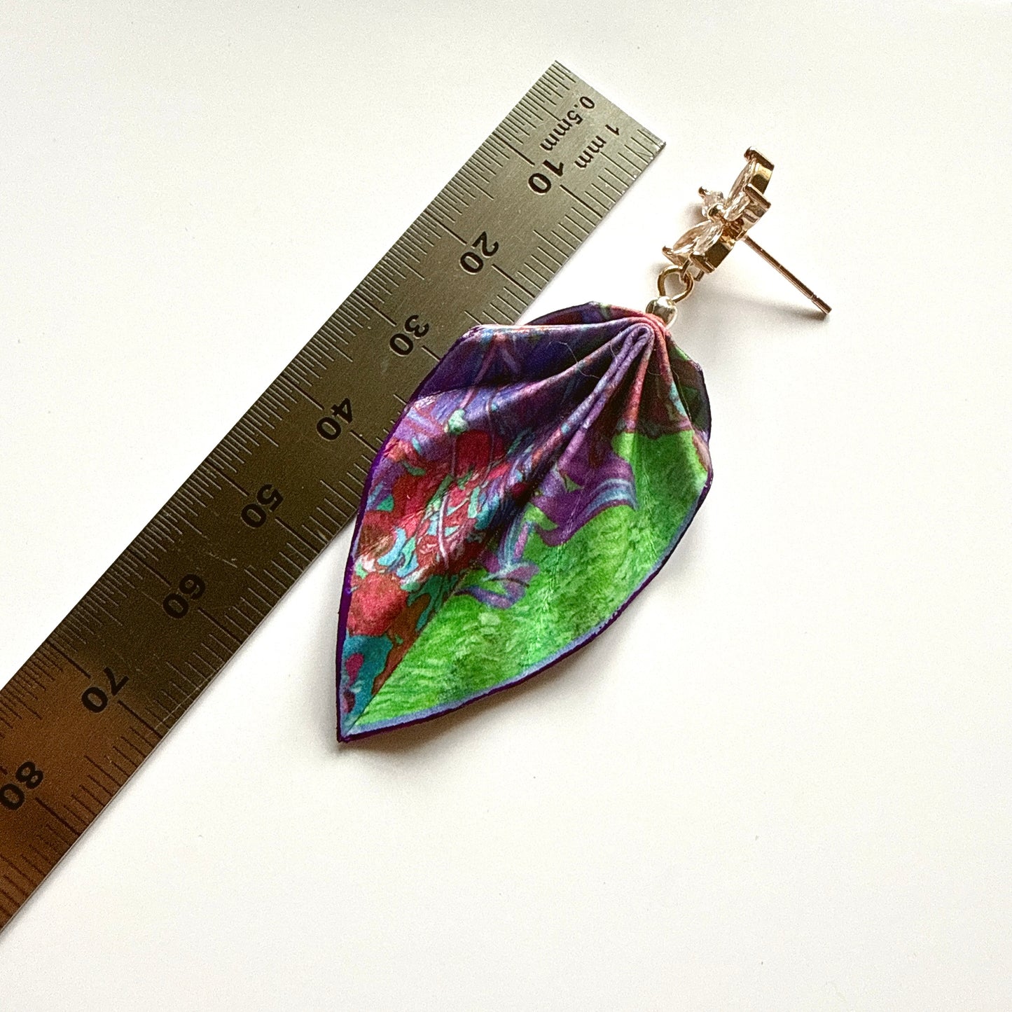Leaf-shaped earrings with floral design next to a ruler on a white background