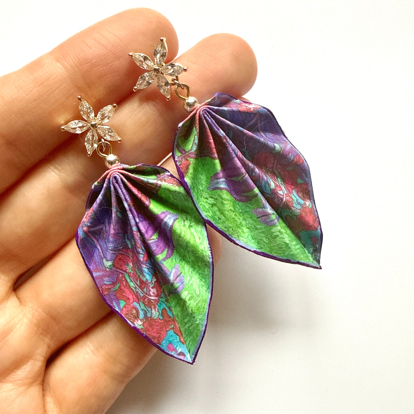 Colorful leaf-shaped earrings held by a hand on a white background