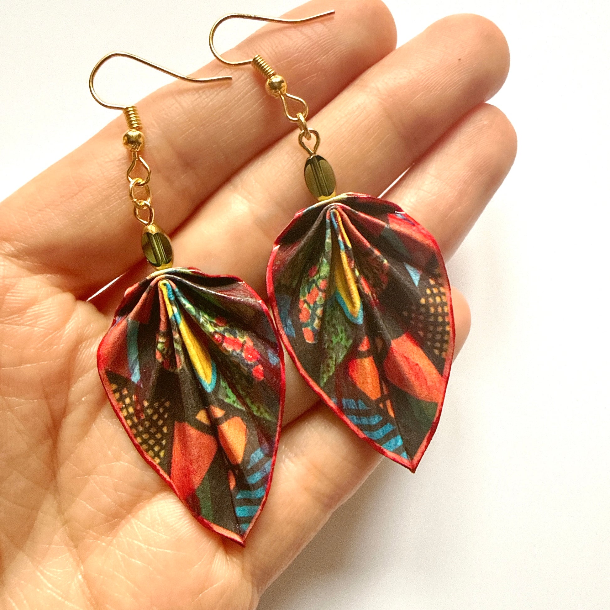 Colorful leaf-shaped earrings held in a hand against a white background