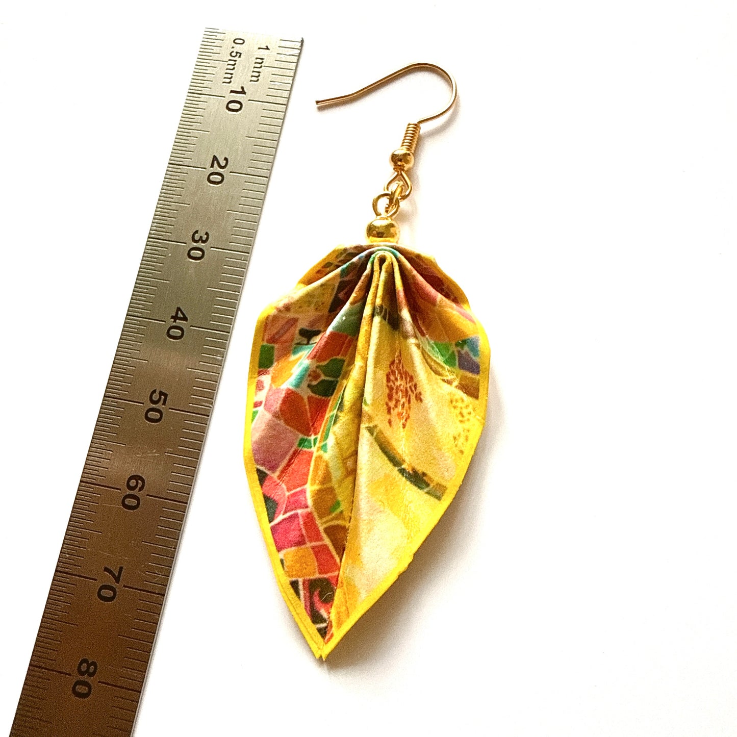 Leaf-shaped earrings with a colorful pattern next to a ruler on a white background