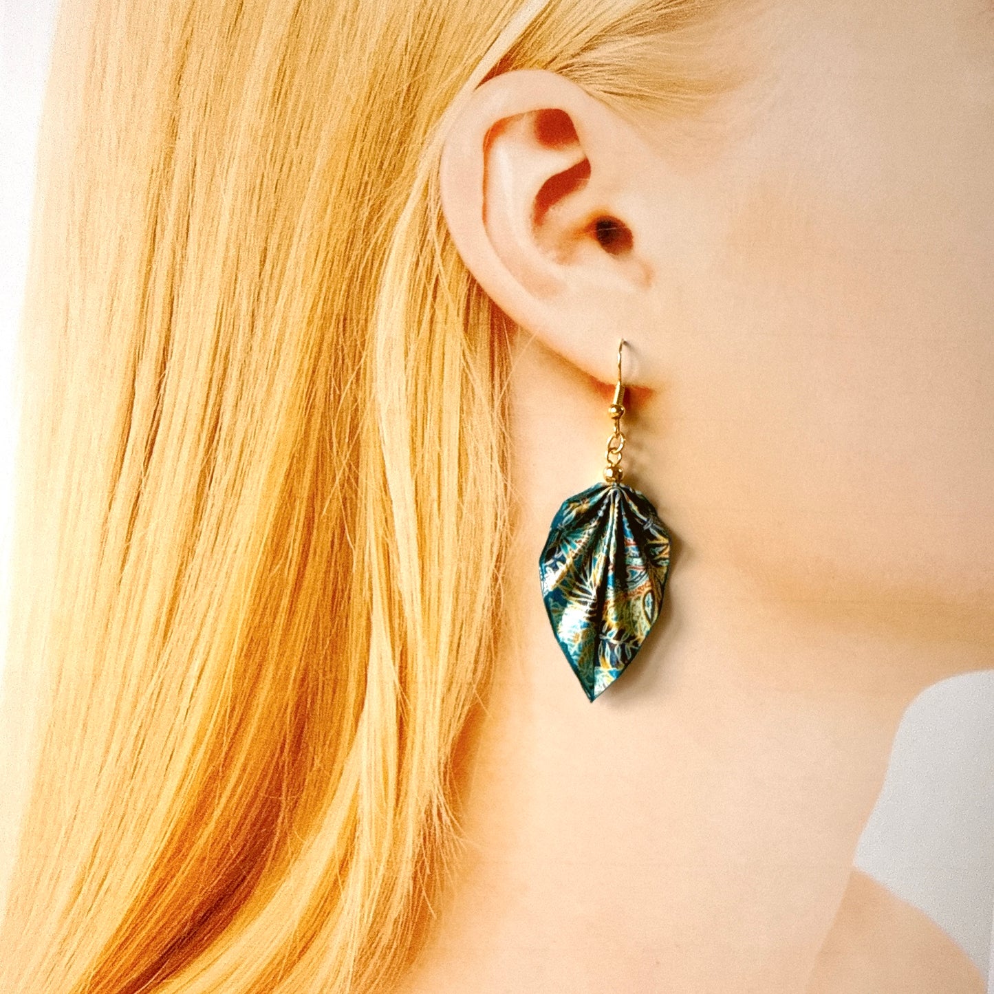 Close-up of a person wearing a leaf-shaped earring with a gold hook.
