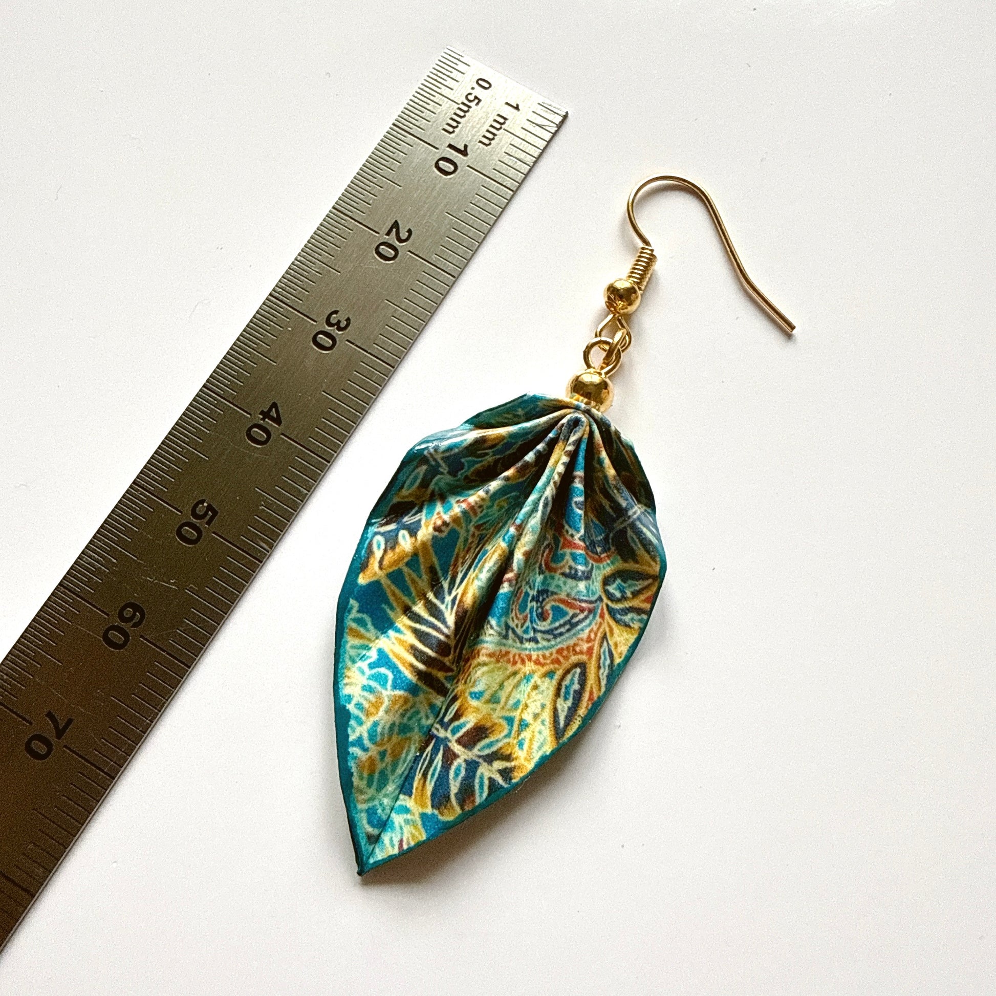 Leaf-shaped earrings with a floral pattern next to a ruler on a white background