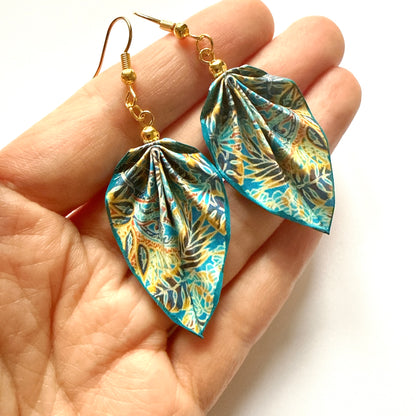 Leaf-shaped earrings with a colorful pattern held in a hand against a white background
