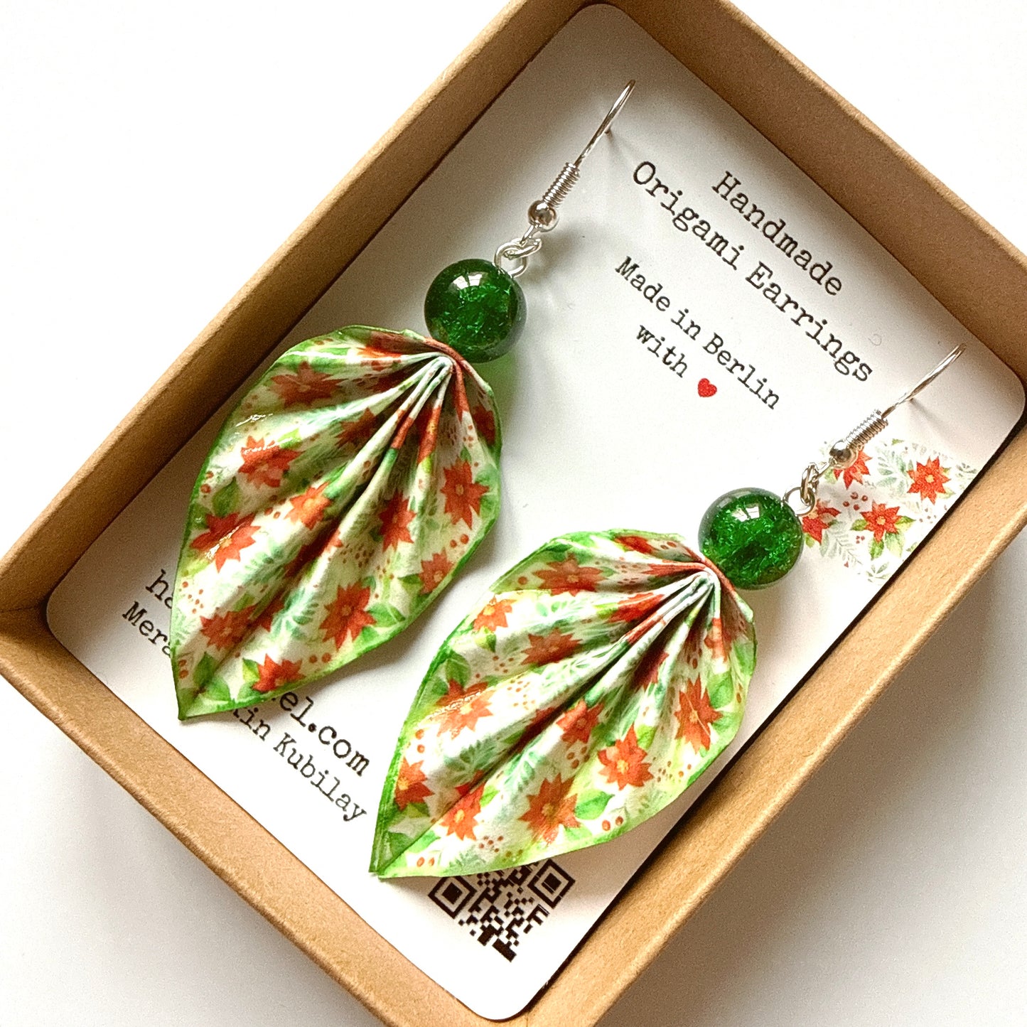 Handmade origami earrings with green and red floral design in a box.