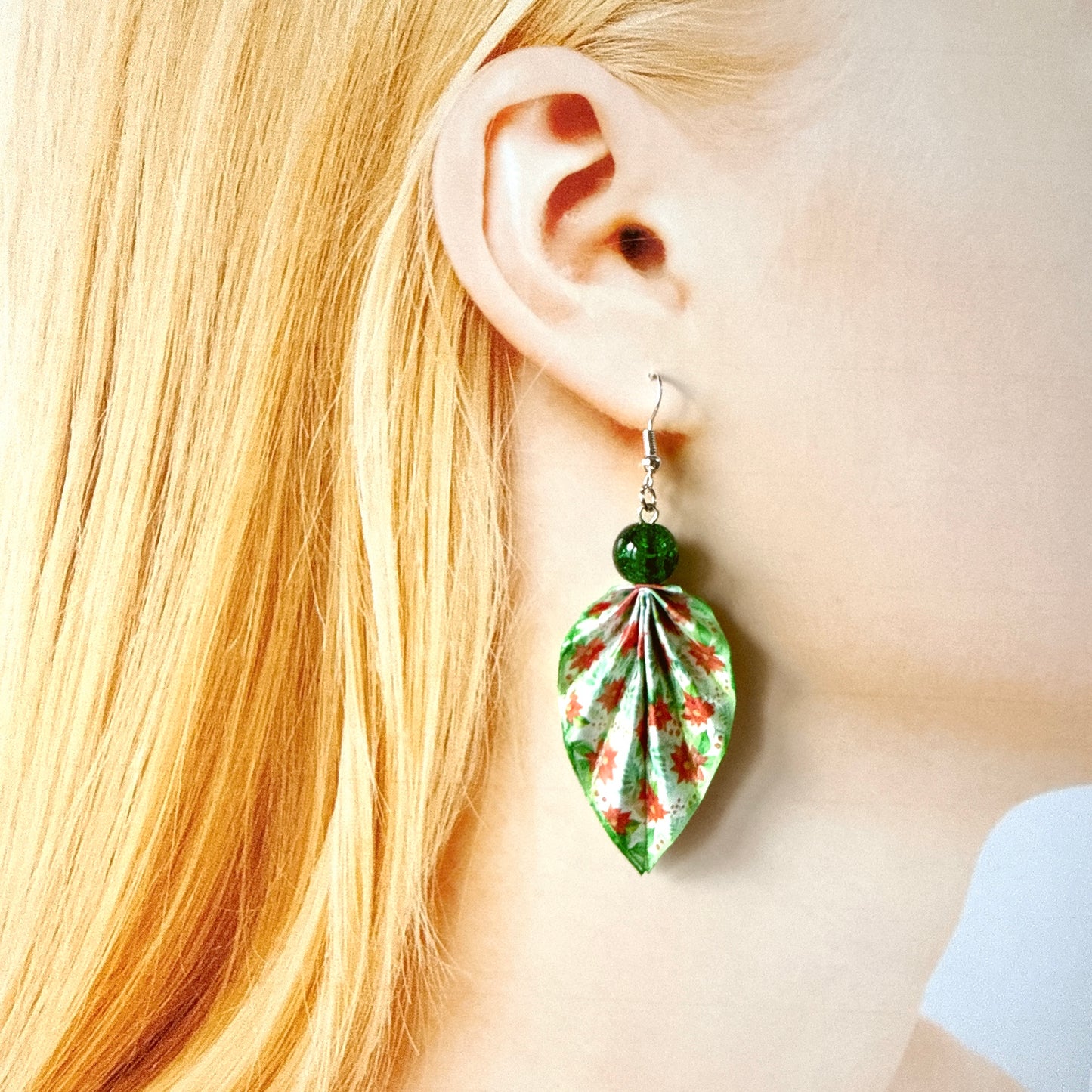 Close-up of a person wearing a green floral earring with blonde hair.