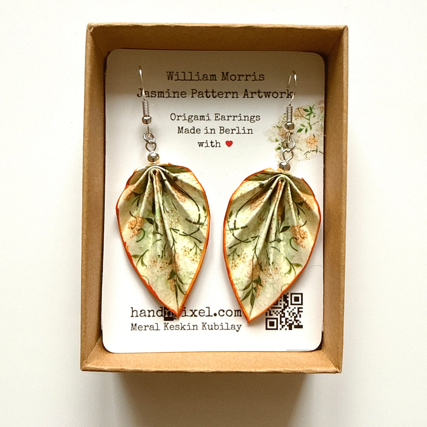 Pair of leaf-shaped earrings with floral design in a box with branding information.