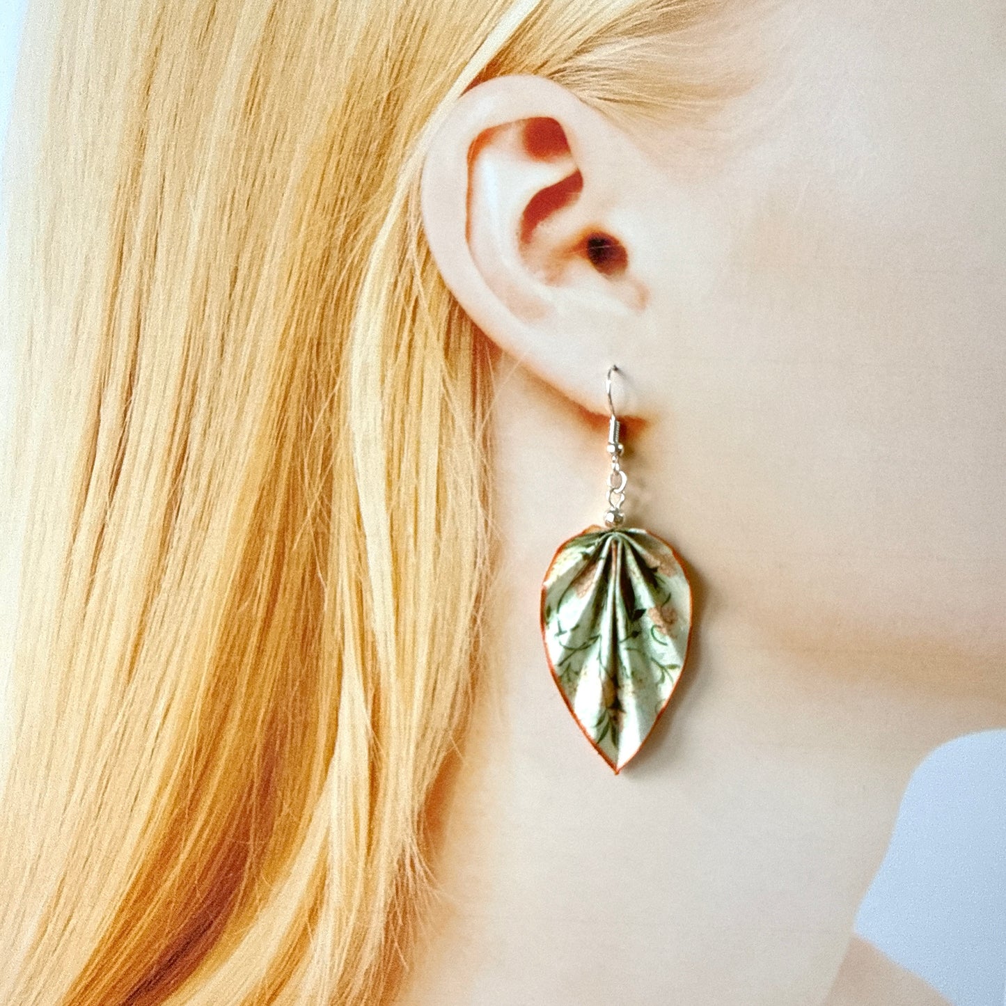 Close-up of a person wearing a leaf-shaped earring with blonde hair.