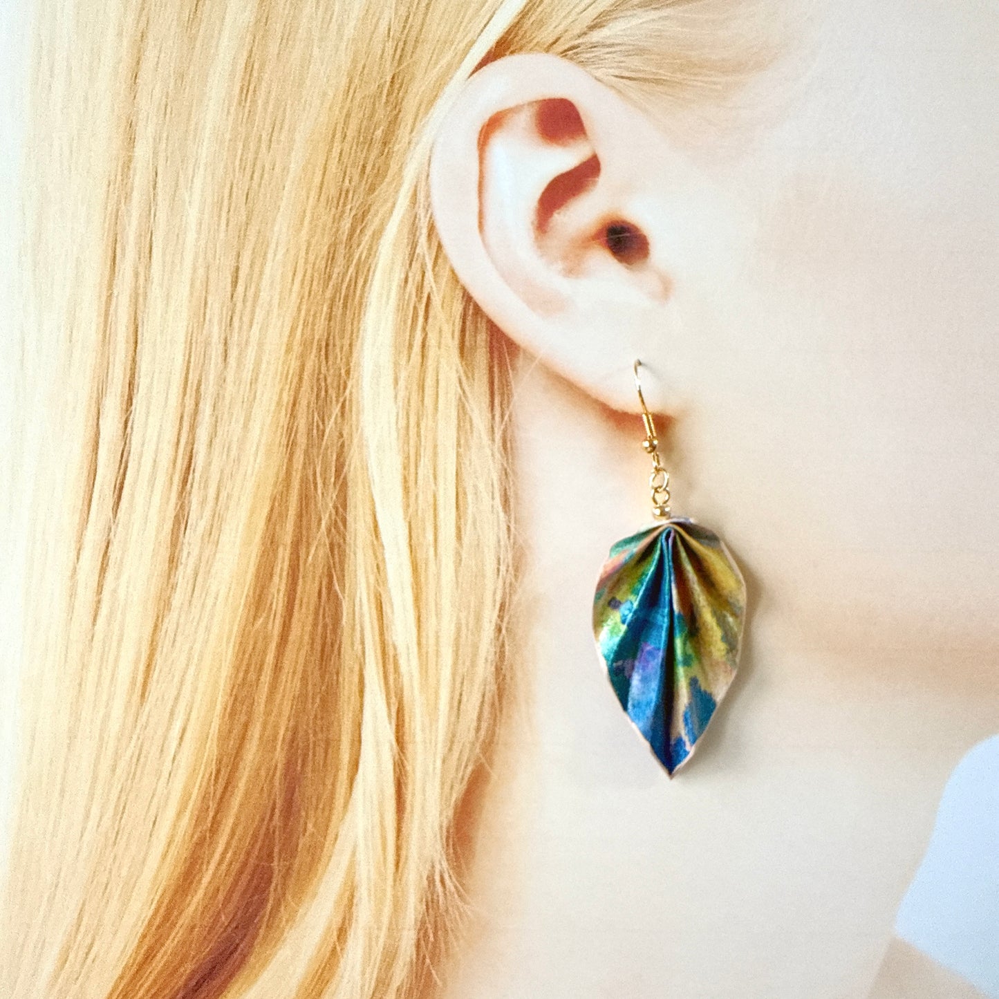 Close-up of a person wearing a colorful leaf-shaped earring with blonde hair.