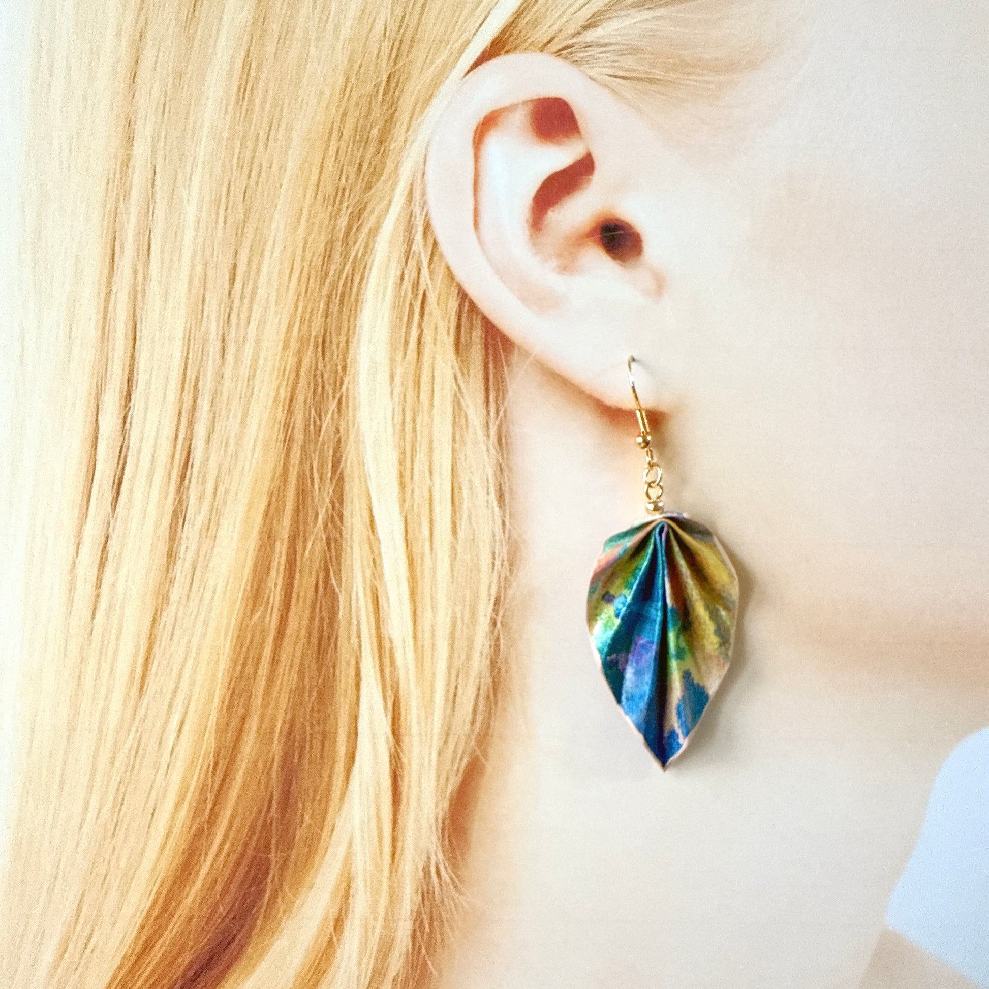 Close-up of a person wearing a colorful leaf-shaped earring with blonde hair.