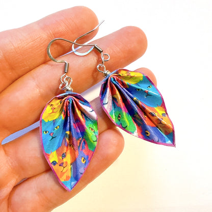 Colorful cat-themed earrings held between fingers against a white background
