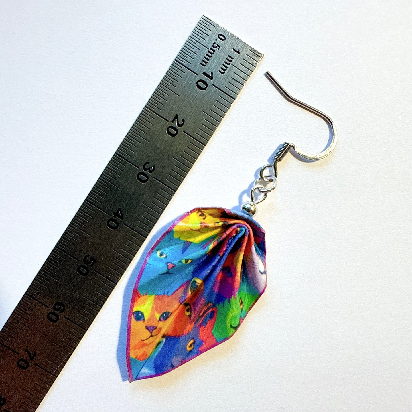 Colorful cat-themed earring next to a ruler on a white background