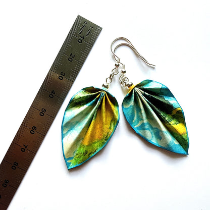 Metallic leaf-shaped earrings with a ruler for scale on a white background