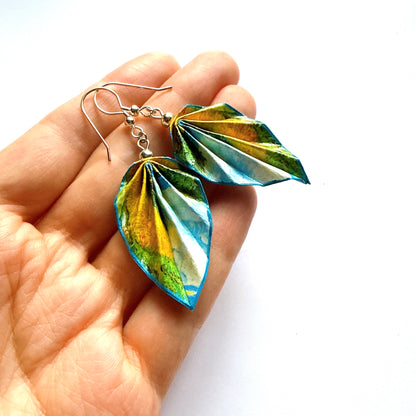 Hand holding a pair of colorful leaf-shaped earrings against a white background