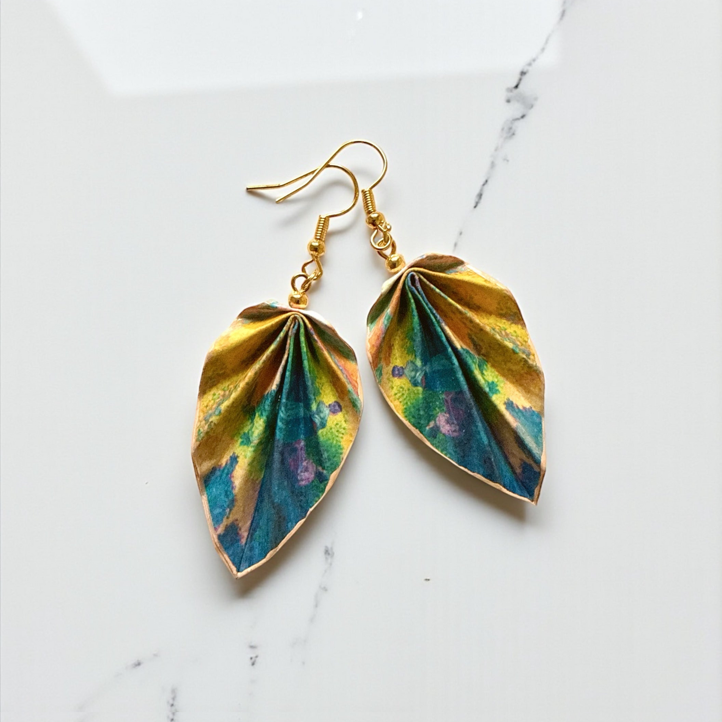 Gold and multicolored leaf-shaped earrings on a marble surface