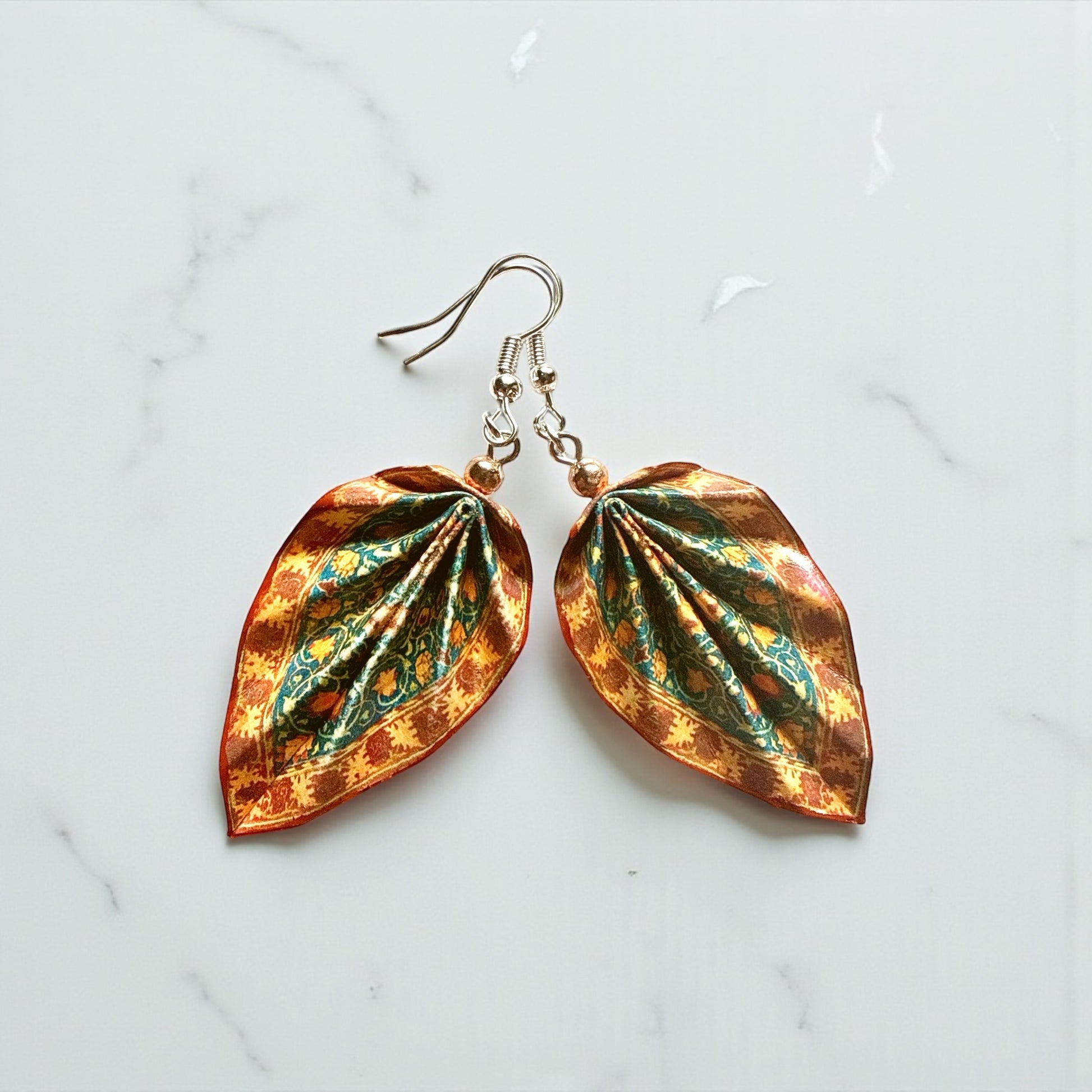 Leaf-shaped earrings with a metallic finish on a light marble background