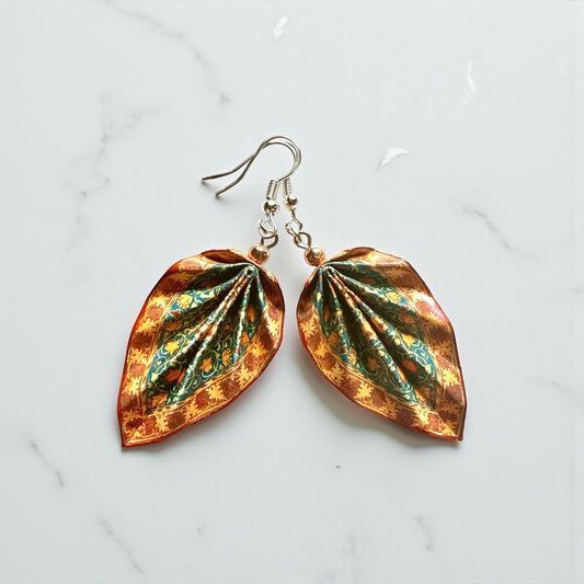 Leaf-shaped earrings with a metallic finish on a light marble background