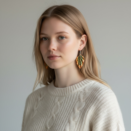 Woman wearing a beige sweater and leaf-shaped earrings against a plain background